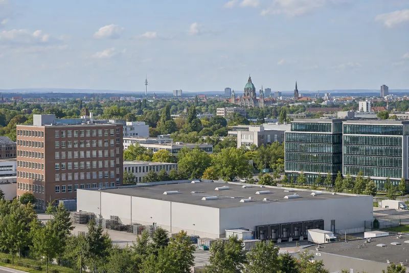Gewerbegebiet bei Hannover mit Backstein-Bürohaus, Glasneubau und Lagerhalle, am Horizont die Silhouette der Stadt