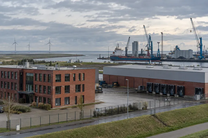 Backsteinbetriebsgebäude und Lagerhalle am Hafenrand in Küstenlage mit Kränen und Windrädern im Hintergrund
