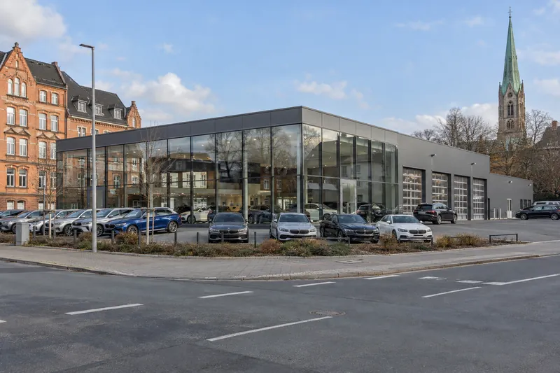 Autohaus mit Glas-Schauraum und angebauter Werkstatt an einer Gewerbestraße in Braunschweig, im Hintergrund Backsteinbauten und ein Kirchturm