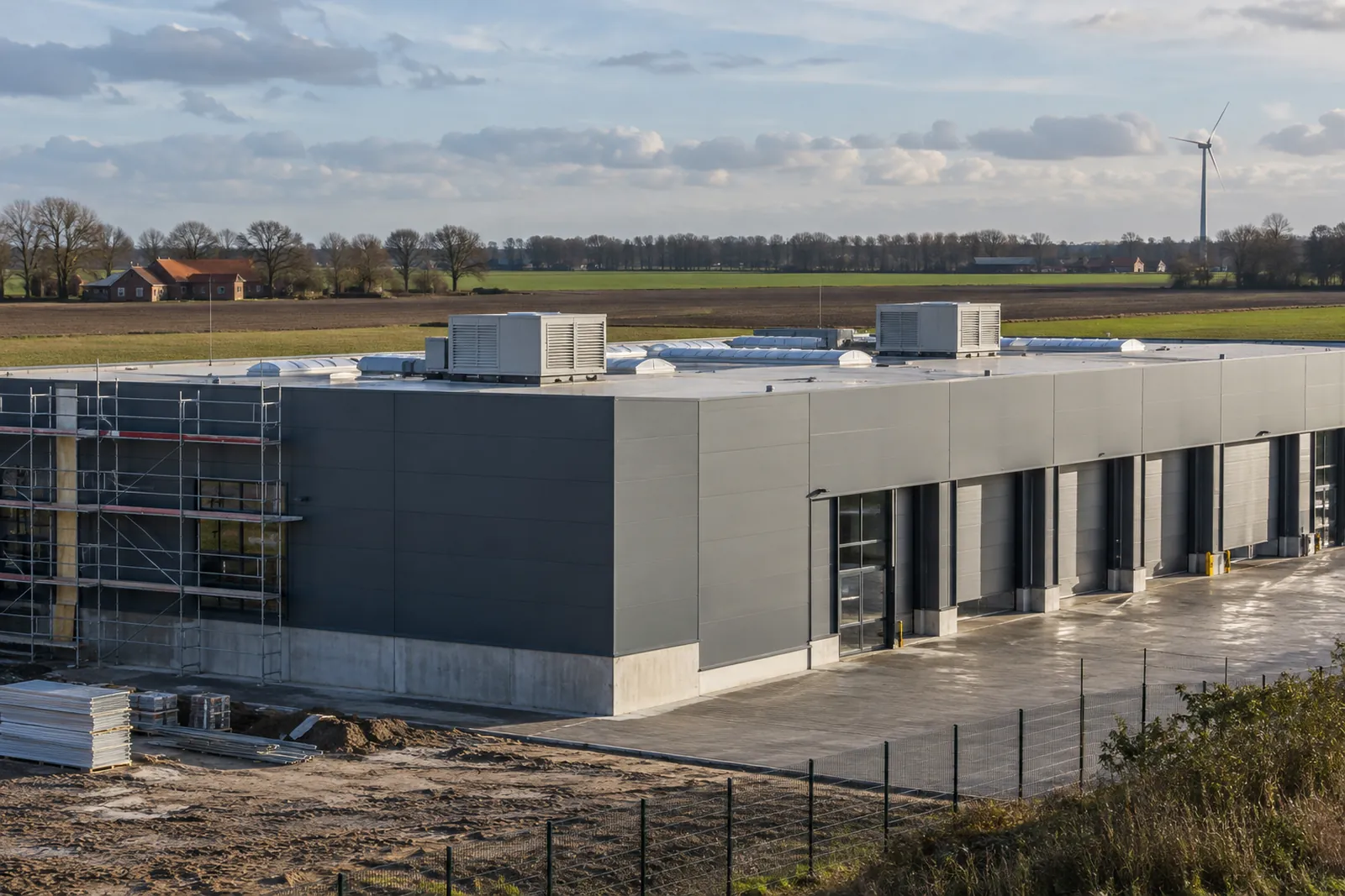 Sanierte Lagerhalle mit neuer Fassadendämmung und Lüftungsgeräten auf dem Dach vor flacher Agrarlandschaft im Oldenburger Münsterland