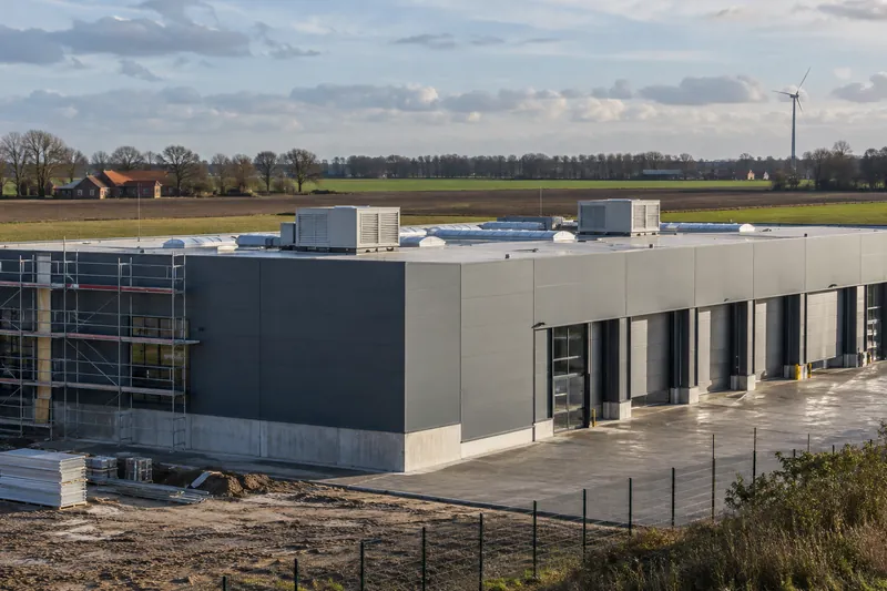 Sanierte Lagerhalle mit neuer Fassadendämmung und Lüftungsgeräten auf dem Dach vor flacher Agrarlandschaft im Oldenburger Münsterland