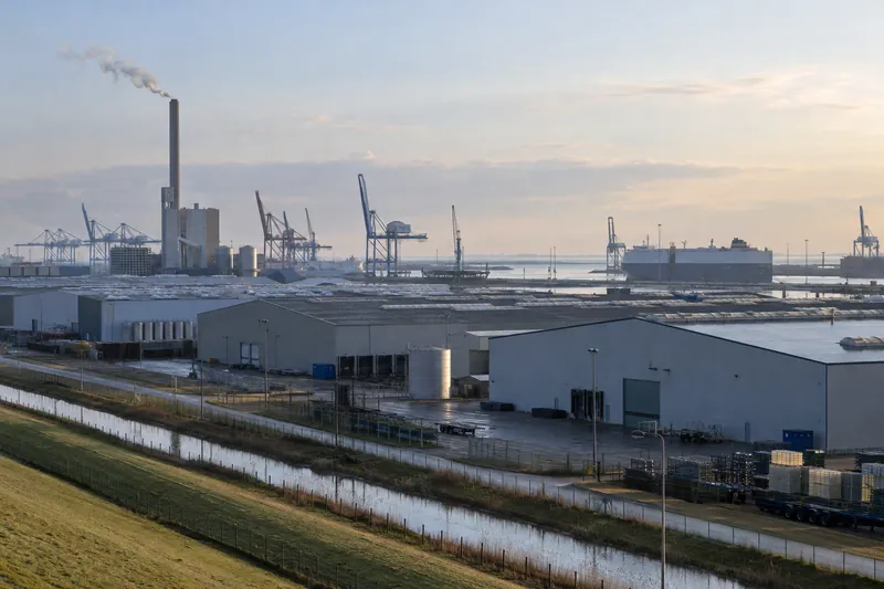 Lagerhallen und Schornstein im Hafengewerbegebiet von Emden mit Kränen im Hintergrund
