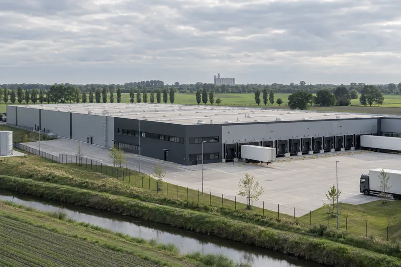 Logistikhalle mit Laderampen auf flachem Gewerbegrundstück im Oldenburger Münsterland, dahinter Ackerland und ein Getreidesilo