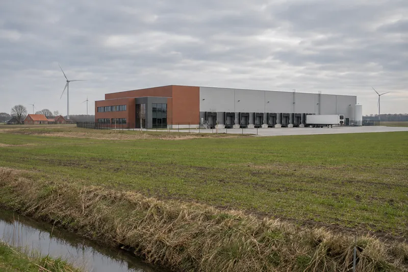 Kühl- und Logistikhalle in der flachen Agrarlandschaft bei Vechta mit Verladetoren und Windrädern am Horizont