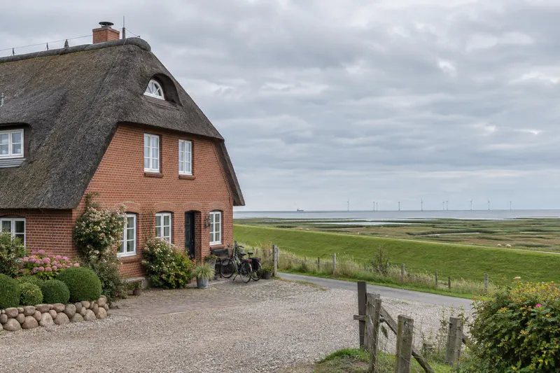 Backsteinpension an der niedersächsischen Nordseeküste mit Deich und Windrädern im Hintergrund