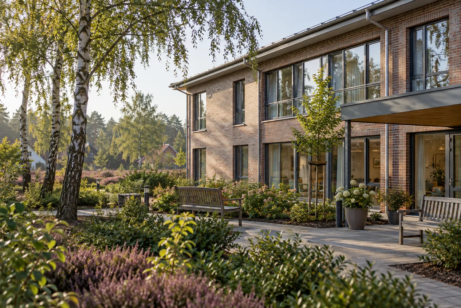 Zweigeschossiges Pflegeheim mit Backsteinfassade und Garten, im Hintergrund Birken und niedrige Heide