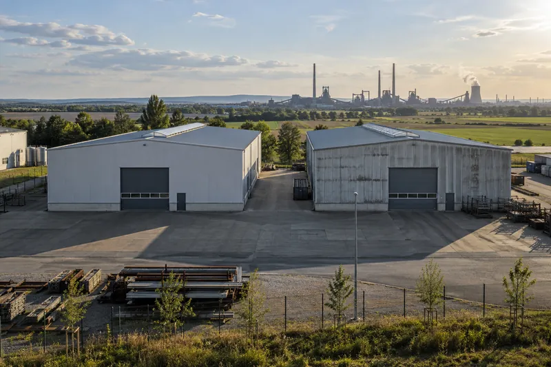 Zwei gleich große Gewerbehallen nebeneinander in einem Gewerbegebiet bei Salzgitter, im Hintergrund Industrieschornsteine