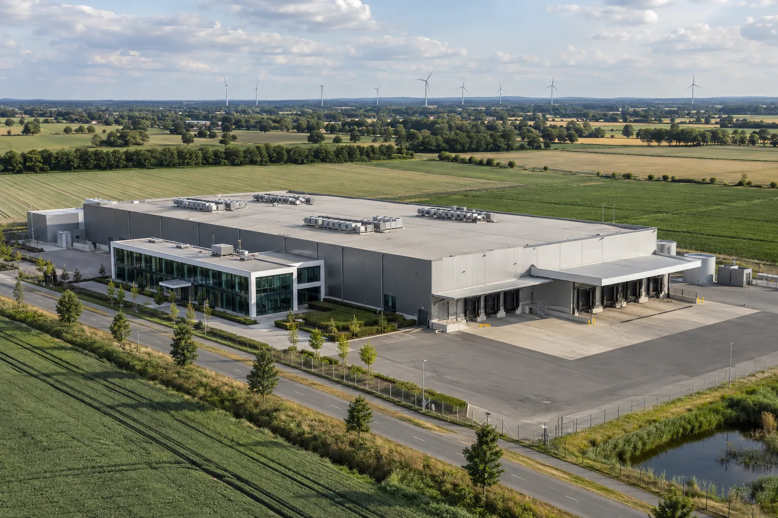 Kühllagerhalle mit Büroanbau und Verladerampe in flacher Landschaft bei Vechta, im Hintergrund Windräder