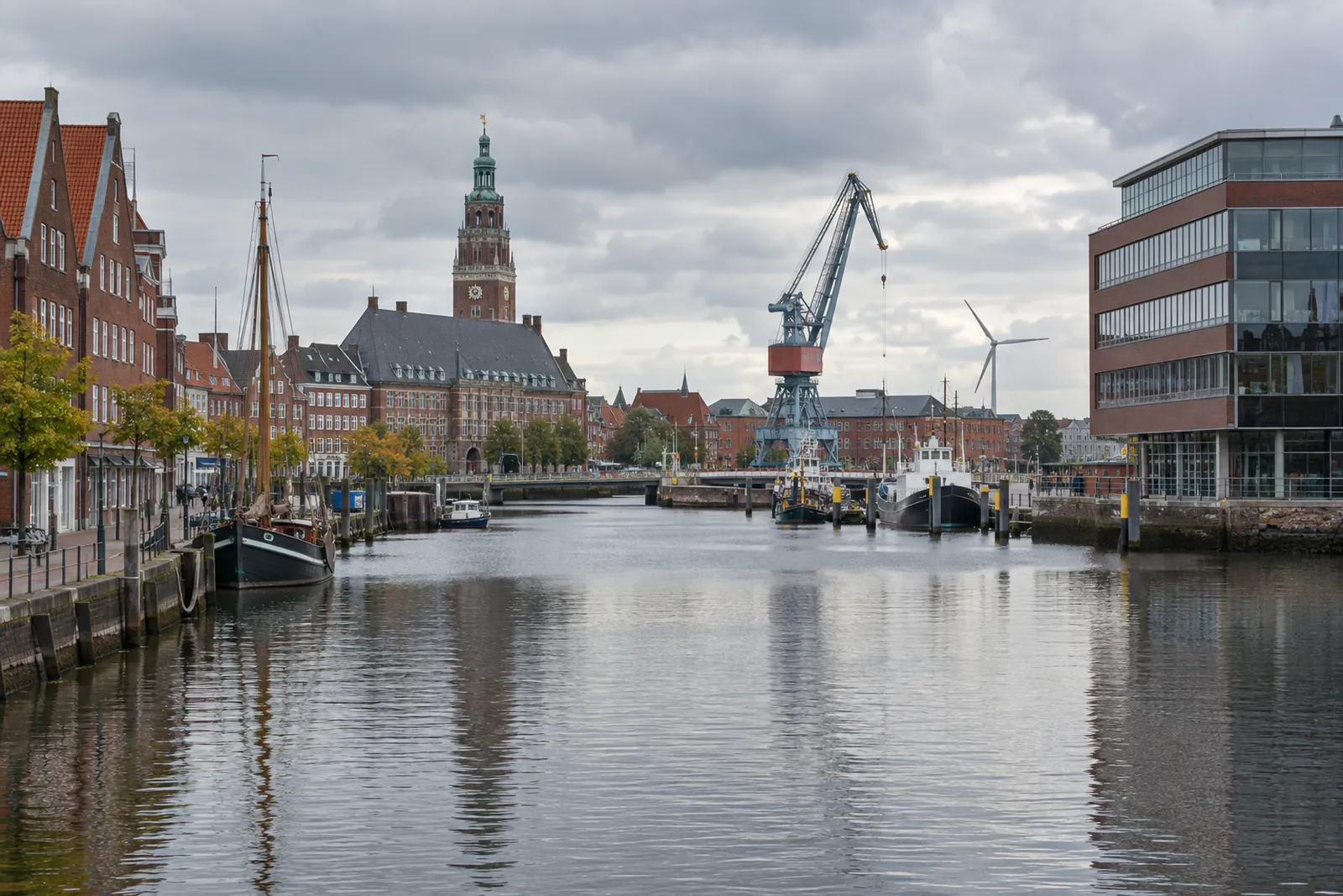 Backsteinbauten und ein Bürogebäude am Ratsdelft in Emden, im Hintergrund Rathausturm, Hafenkran und Windrad