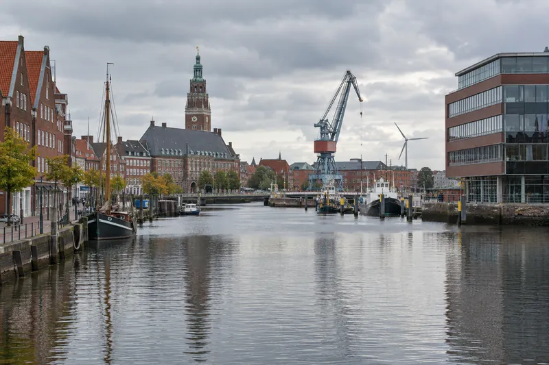Backsteinbauten und ein Bürogebäude am Ratsdelft in Emden, im Hintergrund Rathausturm, Hafenkran und Windrad