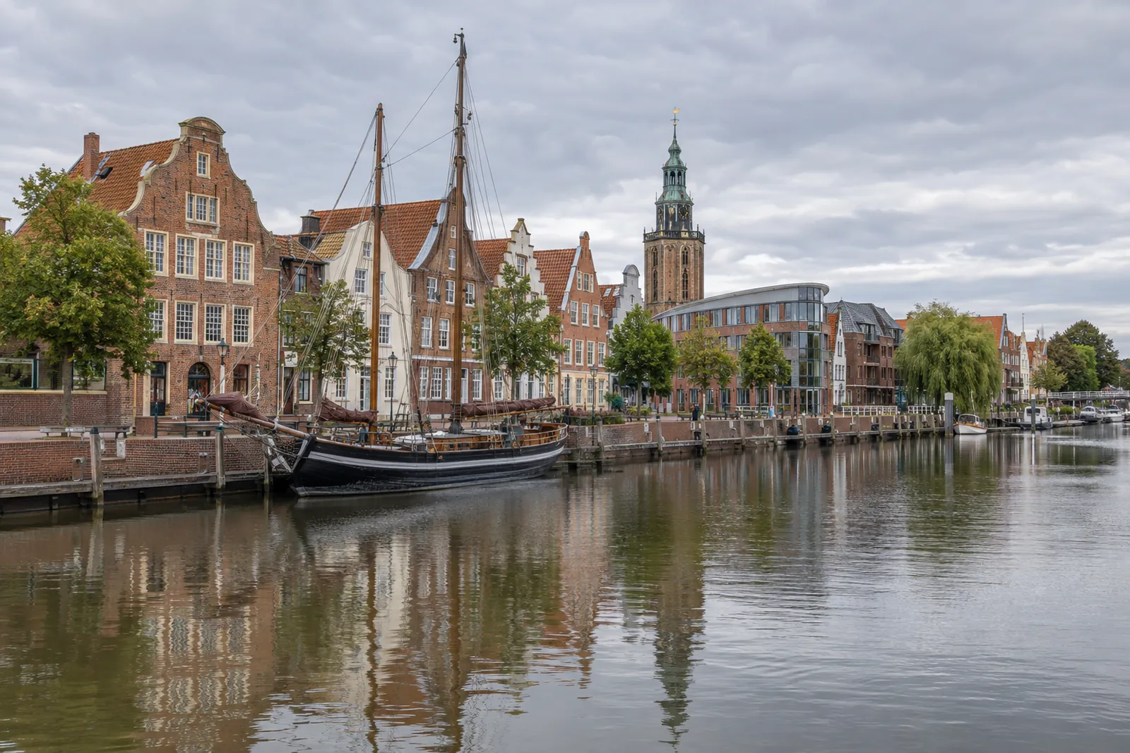 Historische Giebelhäuser am Hafen in Leer mit Museumsschiff, Bürogebäude und Rathausturm im Hintergrund
