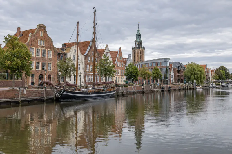 Historische Giebelhäuser am Hafen in Leer mit Museumsschiff, Bürogebäude und Rathausturm im Hintergrund