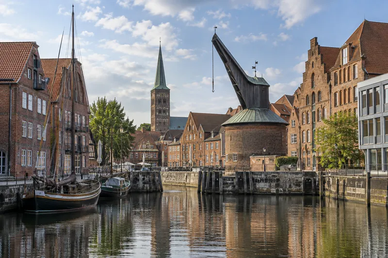 Backsteinspeicher und Giebelhäuser am Hafenbecken einer niedersächsischen Hansestadt mit Kirchturm im Hintergrund