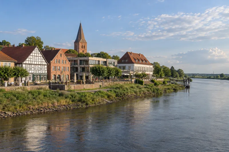 Fachwerk- und Backsteinbauten am Weserufer mit Kirchturm im Hintergrund in einer niedersächsischen Kreisstadt